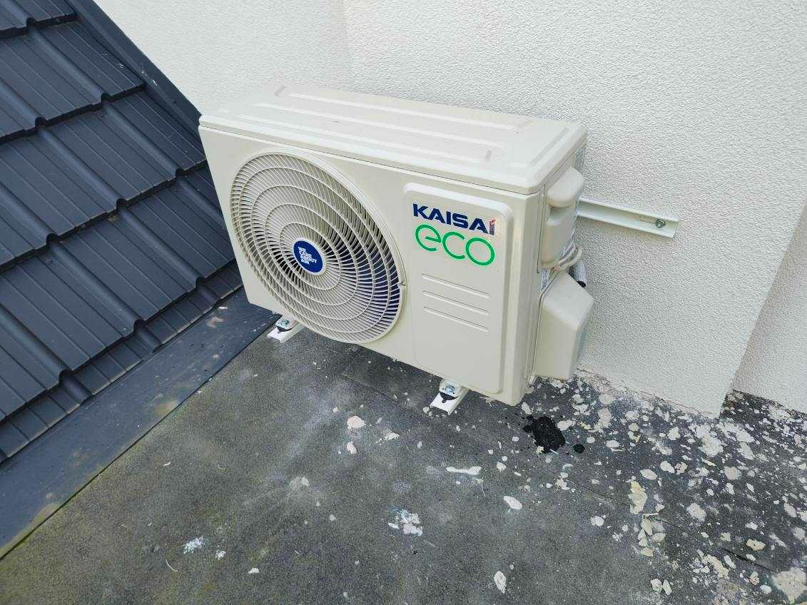 Biała jednostka zewnętrzna klimatyzacji Kaisai Eco zamontowana na dachu przy ścianie budynku.