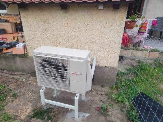 Zewnętrzna jednostka pompy ciepła Atlantic zamontowana na białym stelażu przy elewacji budynku z widocznymi narzędziami i elementami instalacji w tle.