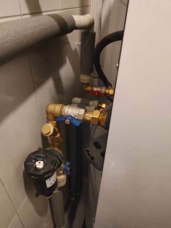 Szczegółowe ujęcie instalacji hydraulicznej z zaworami, rurami izolowanymi i filtrem, prawdopodobnie w kotłowni. Widoczny klucz nastawny obok białej obudowy urządzenia.