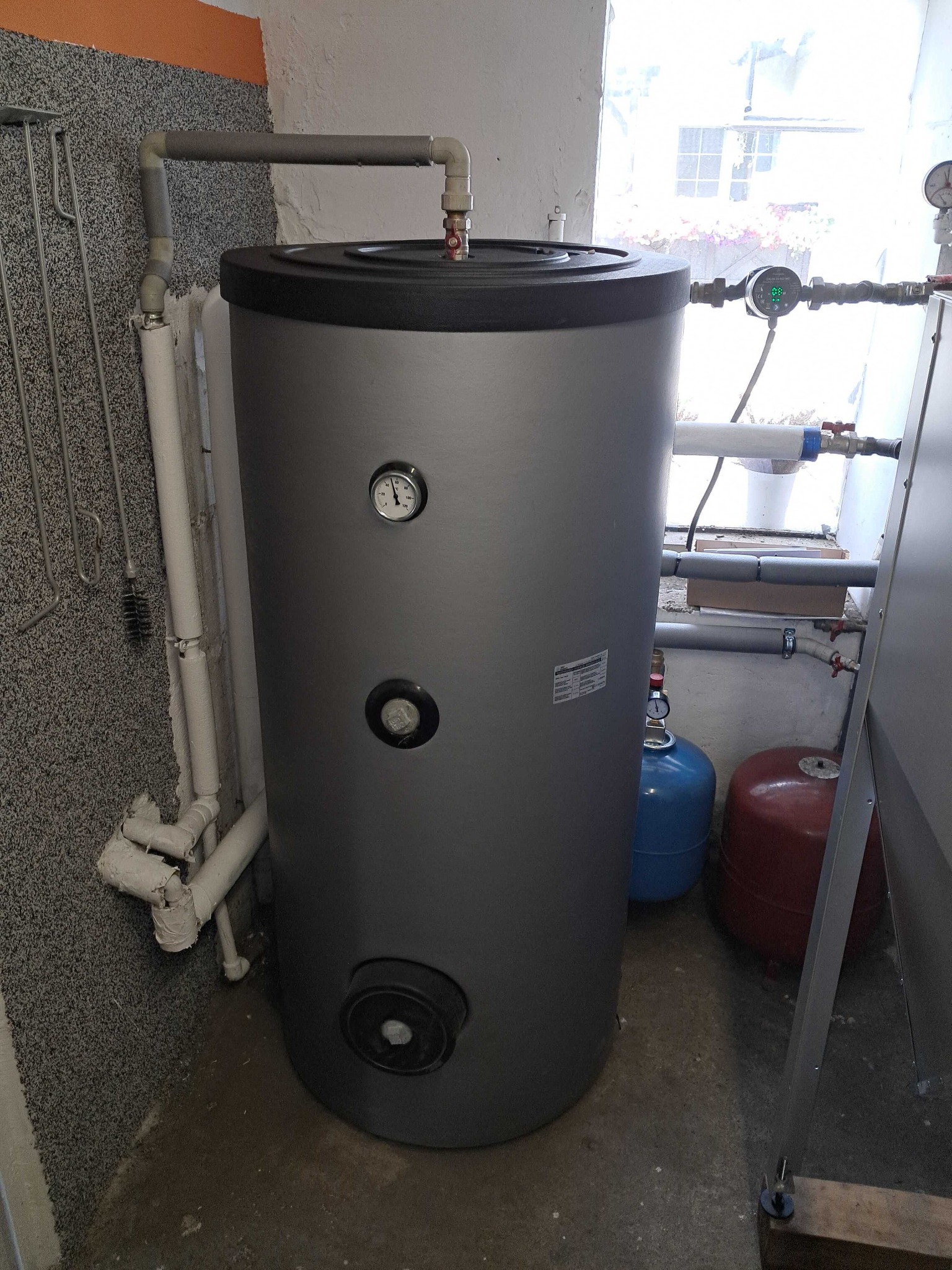 Szary zbiornik akumulacyjny ciepłej wody w kotłowni w Lipnie, widoczne rury, manometry i inne elementy instalacji.