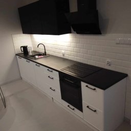 BSOLUTIONS KRZYSZTOF BULBAK - Nowoczesna kuchnia z białymi szafkami, czarnym blatem i płytkami typu metro na ścianie, widoczny czarny okap i płyta indukcyjna.