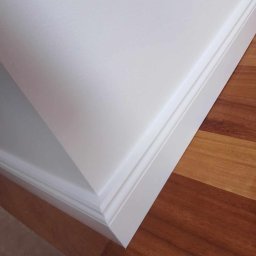 BSOLUTIONS KRZYSZTOF BULBAK - Detale wykończenia wnętrza: biała listwa przypodłogowa z frezowaniem, łącząca ścianę i drewnianą podłogę z wyraźnym usłojeniem.