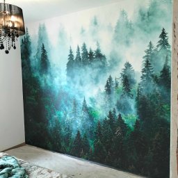 BSOLUTIONS KRZYSZTOF BULBAK - Fototapeta z motywem mglistego lasu iglastego, oświetlona wiszącą lampą z czarnymi kryształkami, na ścianie w trakcie wykańczania.