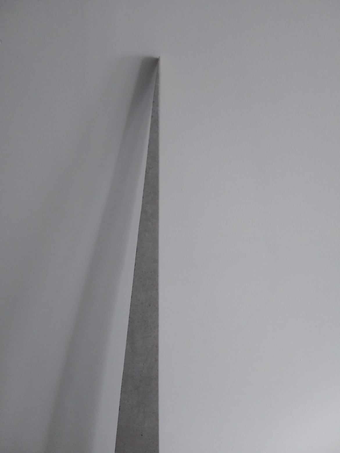 Połączenie dwóch płaszczyzn ścian pod kątem prostym, jedna pomalowana na biało, druga w szarym, surowym wykończeniu, widoczny ostry kant.