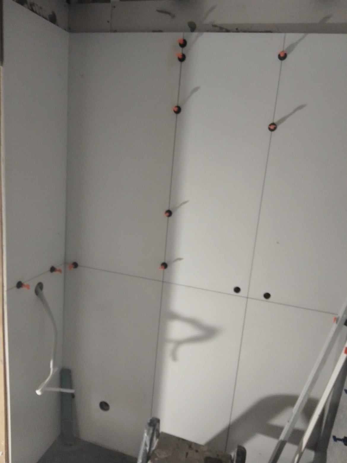 Ściana w trakcie montażu płyt kartonowo-gipsowych, widoczne pionowe linie wyznaczające położenie płyt, czarne znaczniki i otwory na instalacje, fragment drabiny.