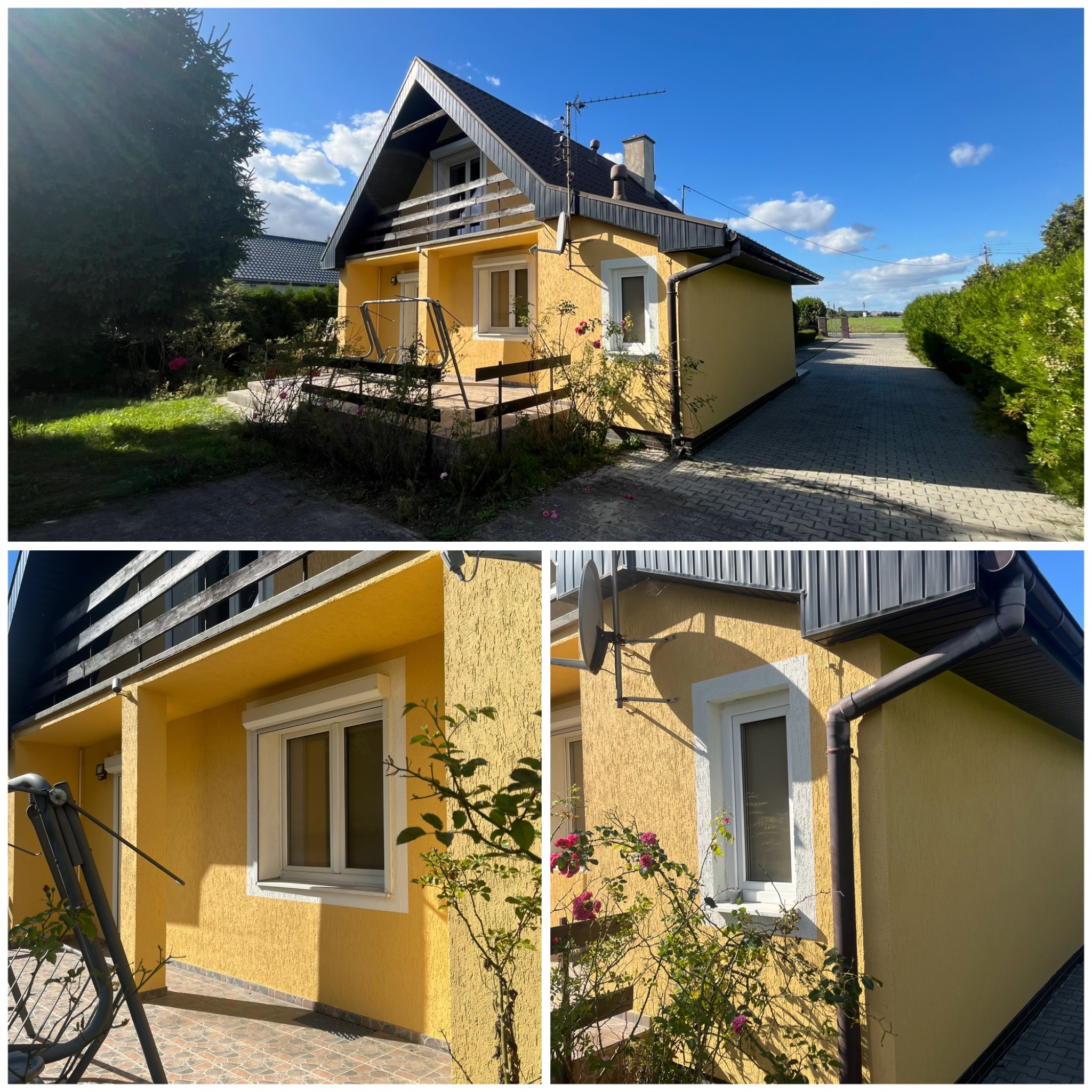 Żółty dom z ciemnym dachem w słoneczny dzień. Widoczna elewacja z fakturą, białe okna i elementy dekoracyjne. Ujęcie z ogrodu, z widoczną roślinnością i ścieżką.