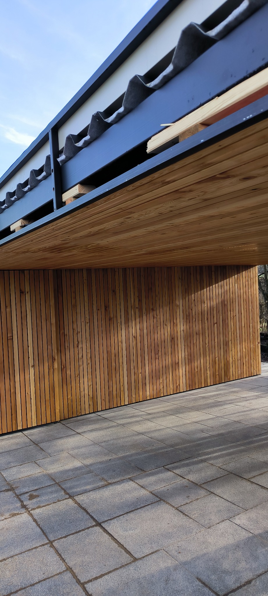 Nowoczesna elewacja z drewnianych paneli w Jeleśni, widok z dołu na fragment dachu i wykończoną ścianę.