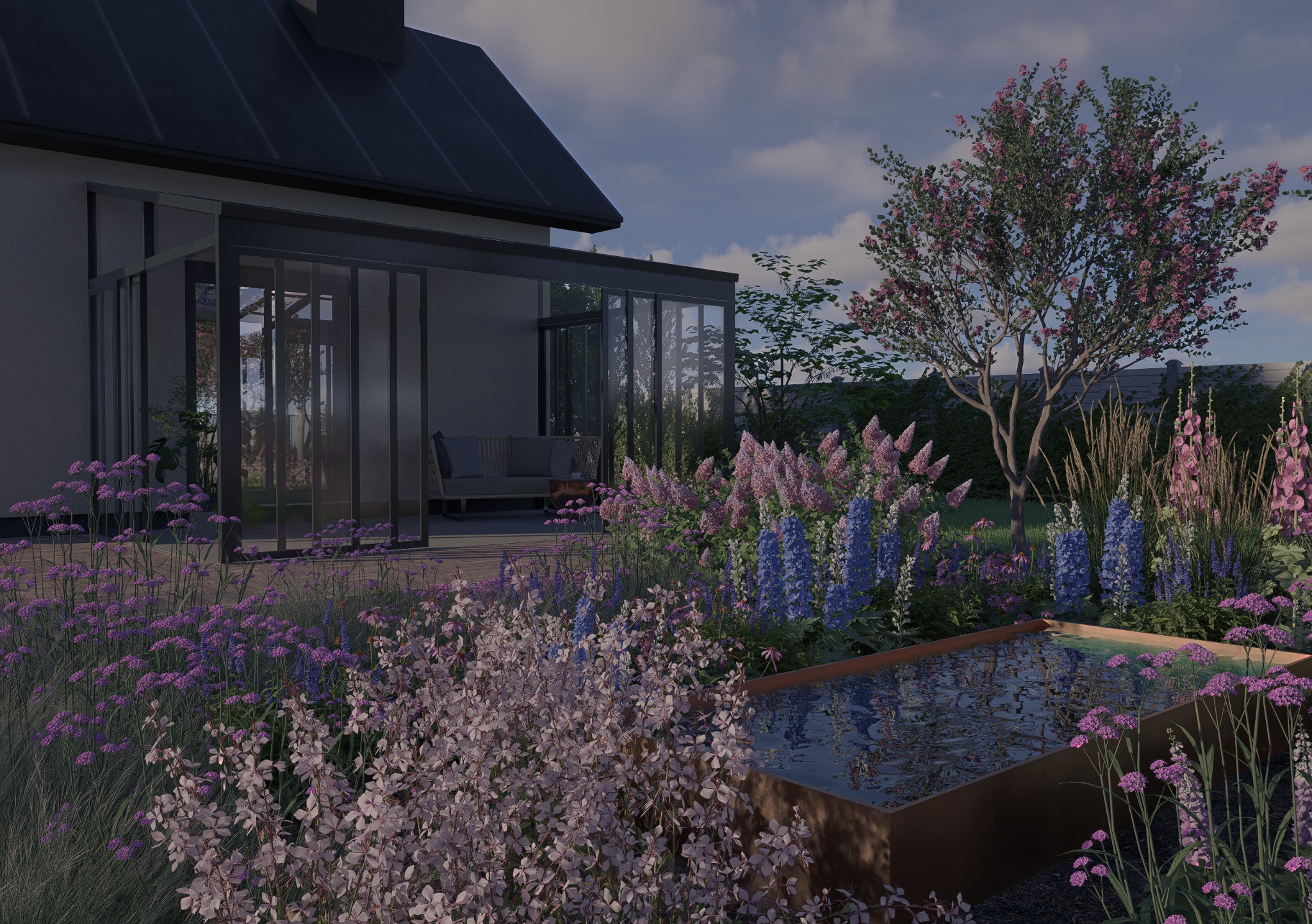 Nowoczesny ogród z kwitnącymi kwiatami i oczkiem wodnym na pierwszym planie, przeszklona weranda domu w tle, drzewo z różowymi kwiatami po prawej stronie.