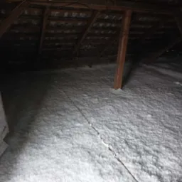 Poddasze po ociepleniu, widoczne drewniane krokwie i słupy, pokryte grubą warstwą białej izolacji.