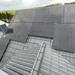 DOM BEZ WAD SPÓŁKA Z OGRANICZONĄ ODPOWIEDZIALNOŚCIĄ - Panele słoneczne zamontowane na szarym dachu domu jednorodzinnego, widok z góry, w tle pole i las