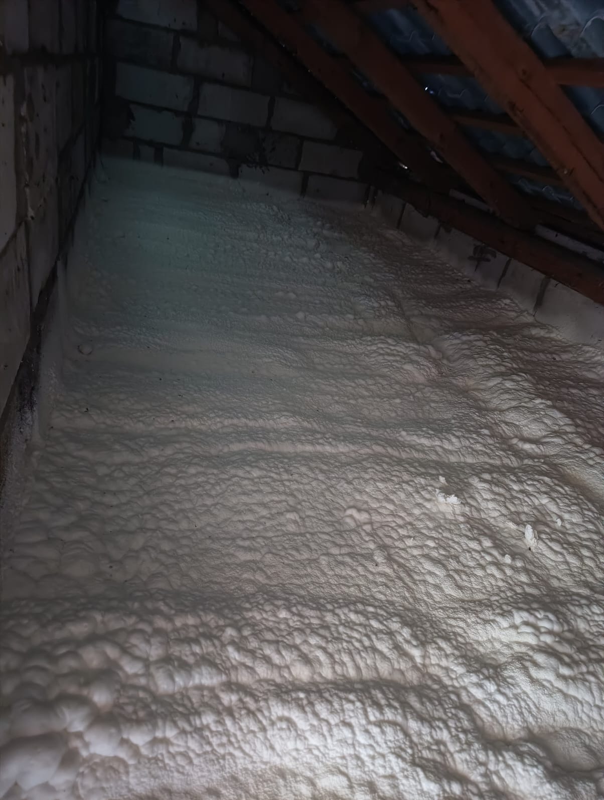 Poddasze ocieplone pianką PUR, widoczne drewniane elementy konstrukcji dachu i fragment ściany z pustaków.