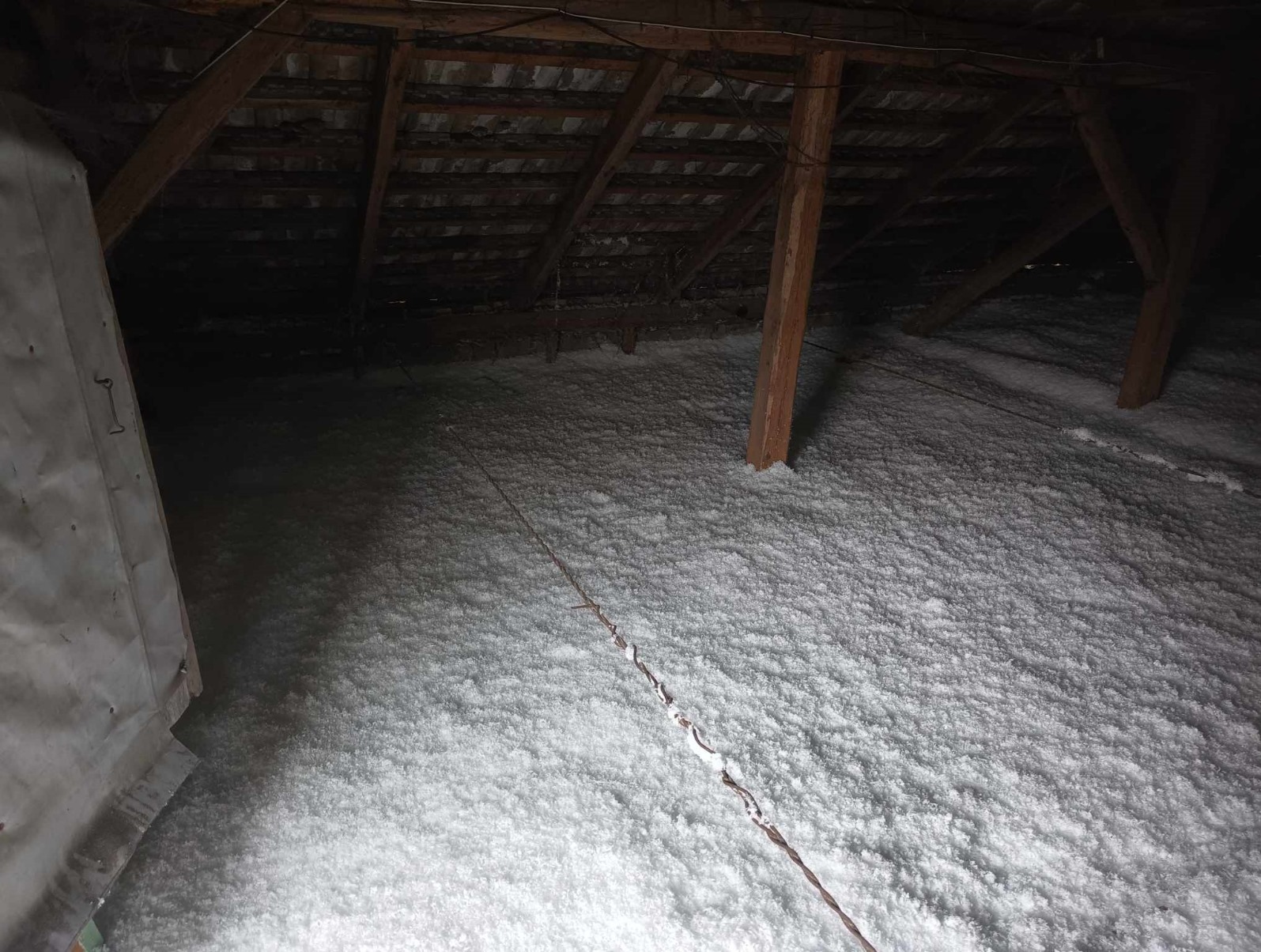 Poddasze po ociepleniu, widoczne drewniane krokwie i słupy, pokryte grubą warstwą białej izolacji.
