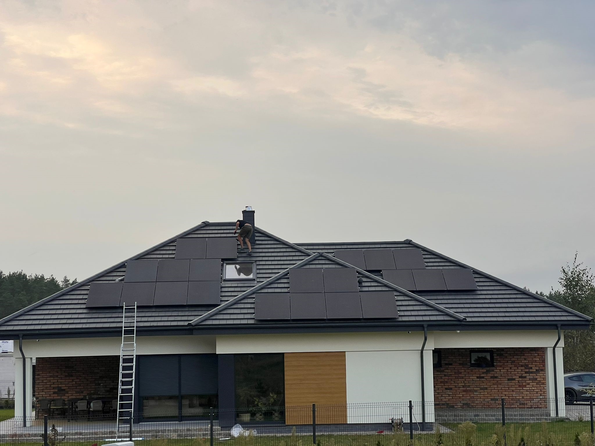 Montaż paneli słonecznych na dachu domu jednorodzinnego z wykorzystaniem drabiny, widoczny pracownik w trakcie instalacji.