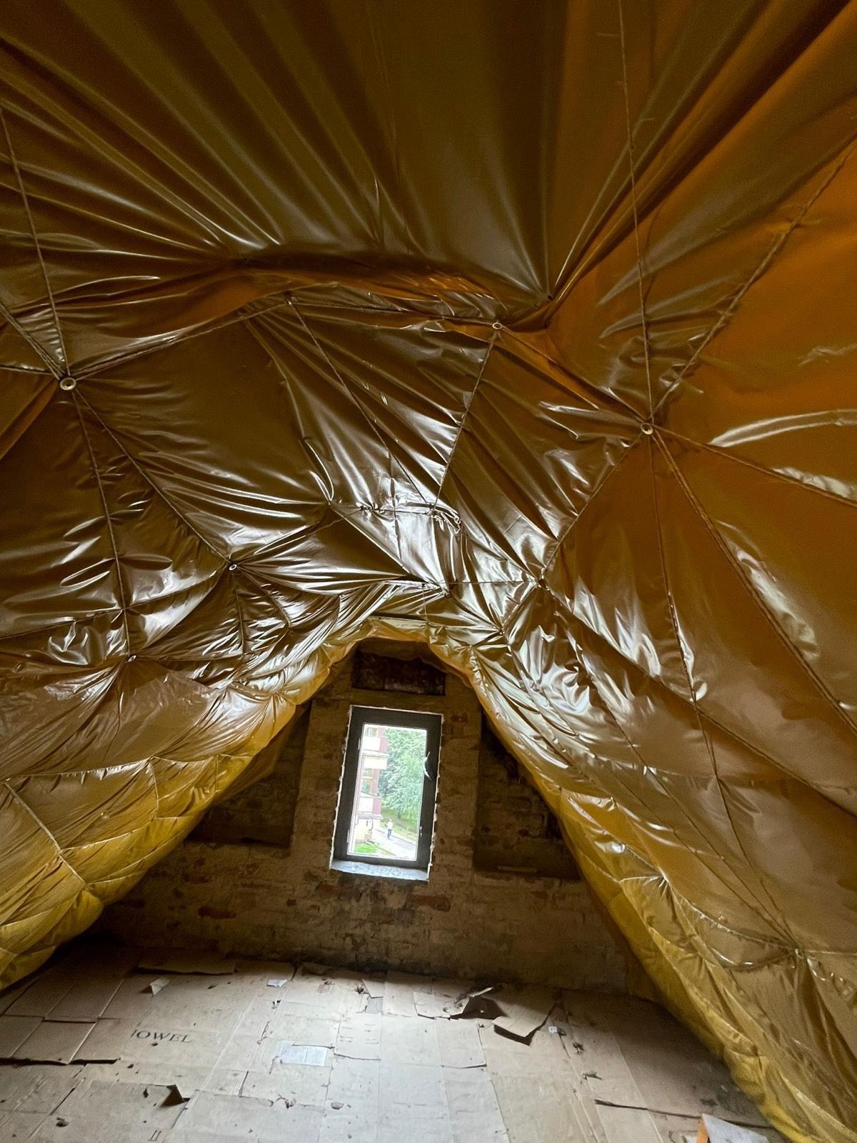 Poddasze zabezpieczone folią paroizolacyjną przed montażem izolacji termicznej, widoczne okno dachowe i surowe ceglane ściany.