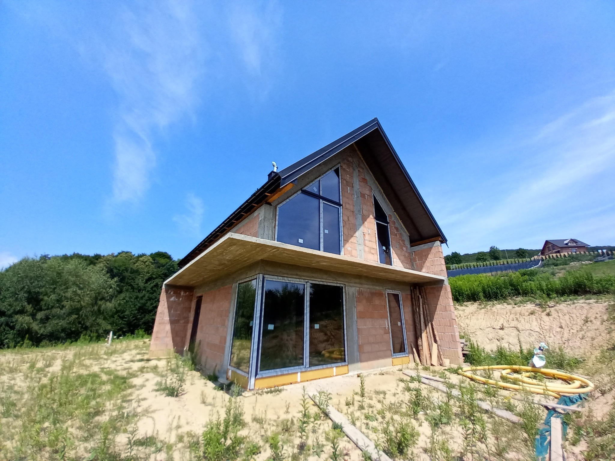 Surowy stan domu z cegły z dużymi oknami, widok z dołu na tle błękitnego nieba, żółty wąż na ziemi, teren piaszczysty.