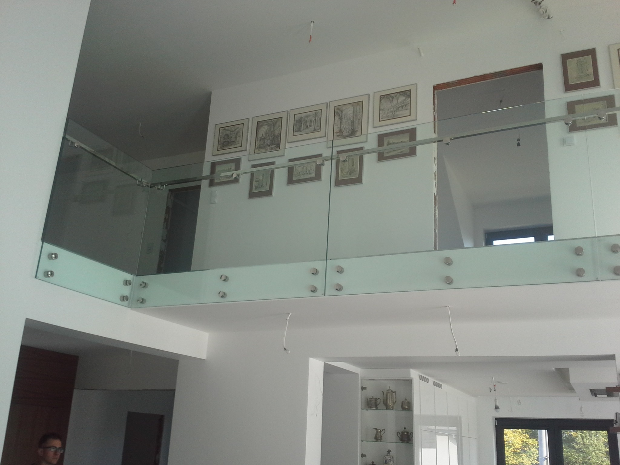 Szklana balustrada na antresoli w domu w Krakowie, mocowana na metalowych uchwytach, widok z dołu na galerię z obrazami.