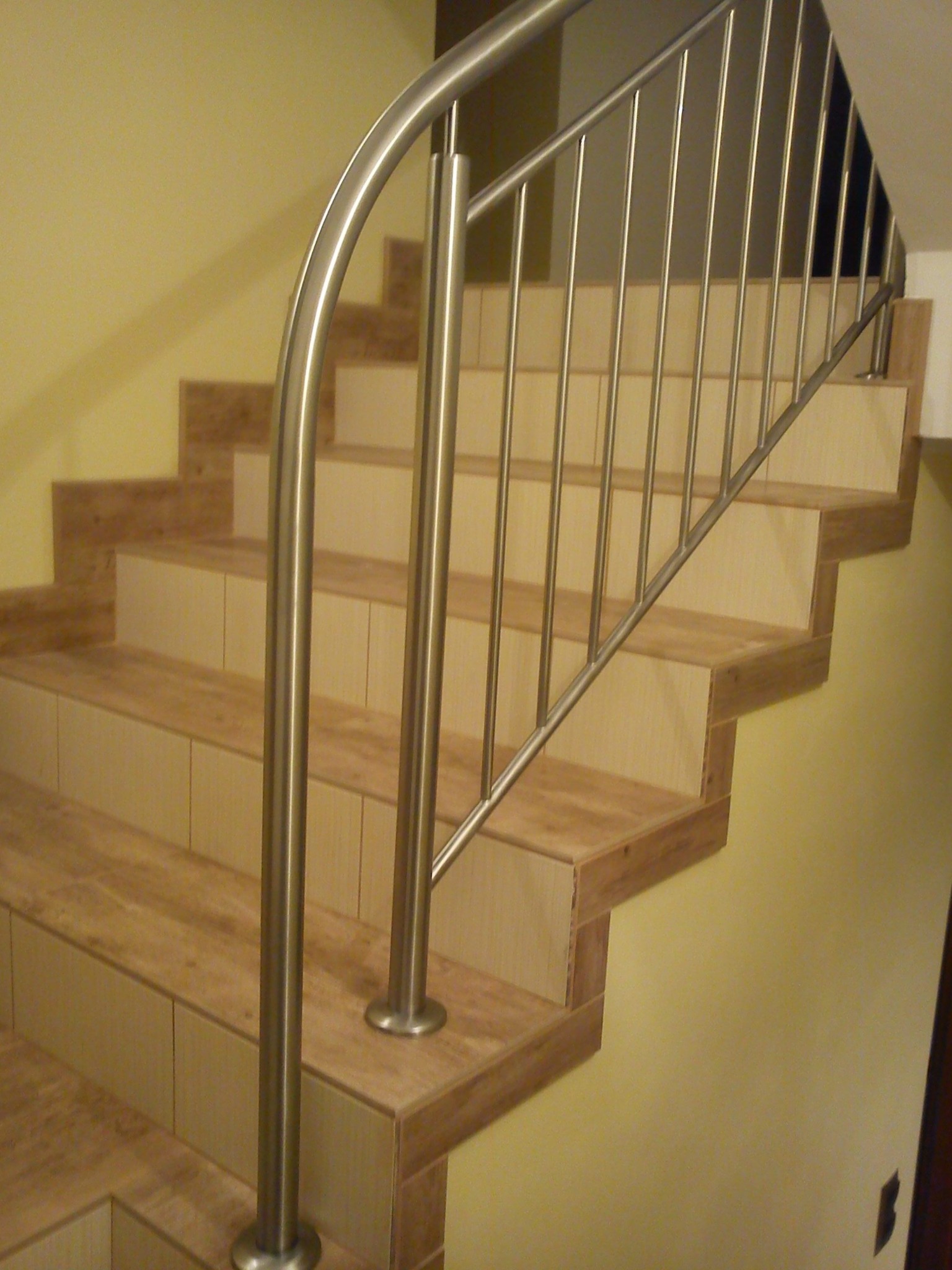 Wewnętrzne schody wykończone płytkami z beżowymi fugami i balustradą ze stali nierdzewnej o okrągłym przekroju, zamontowaną do stopni.