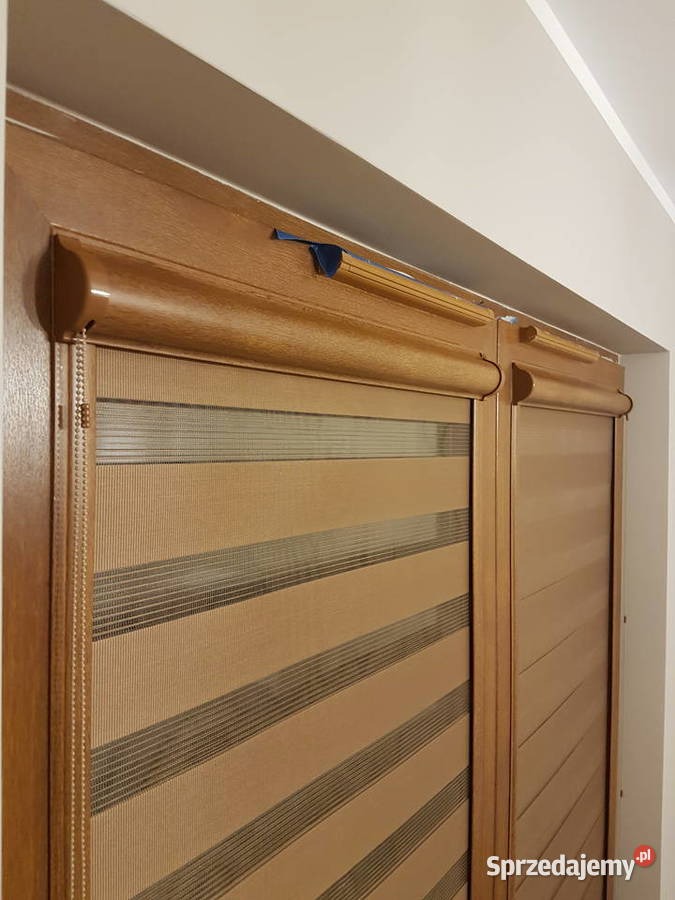 Zamknięte rolety dzień noc w drewnianej ramie okiennej, z widocznym mechanizmem sterującym. Beżowo-brązowe pasy tworzą efekt zaciemnienia.