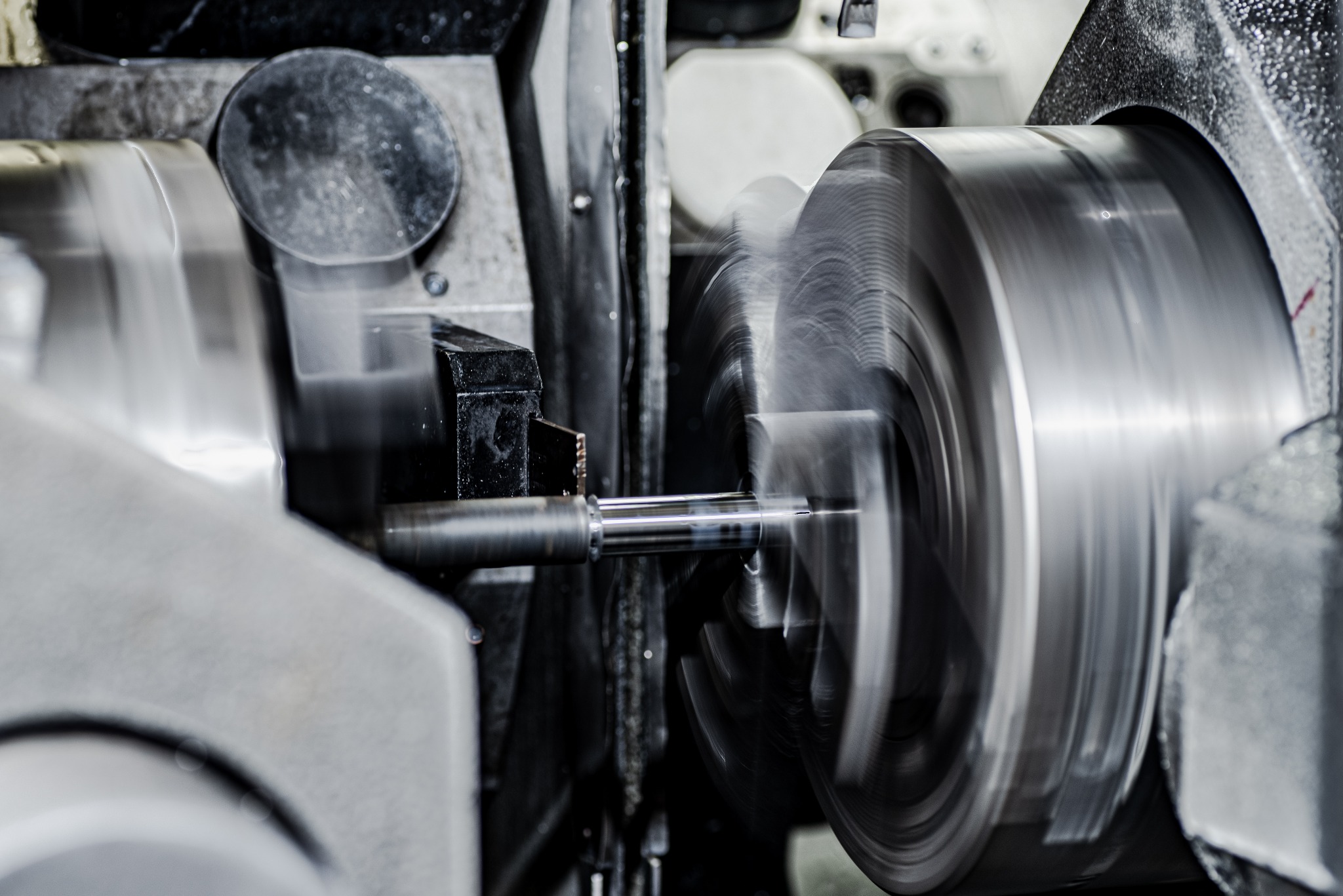 Metalowy wałek obracający się z dużą prędkością wewnątrz maszyny, z widocznymi śladami obróbki na jego powierzchni, oświetlenie punktowe podkreśla ruch obrotowy.