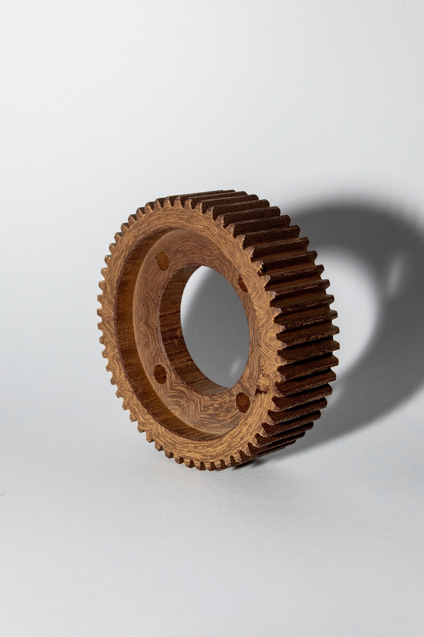 Precyzyjnie wykonane koło zębate z widoczną teksturą materiału, sfotografowane na jasnym tle z wyraźnym cieniem, ukazujące detale obróbki.