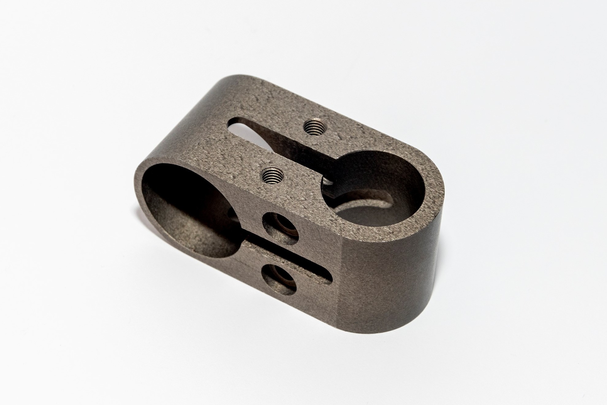 Szary, metalowy element z otworami i gwintowanymi gniazdami na śruby, ułożony na białym tle, widoczne ślady obróbki.