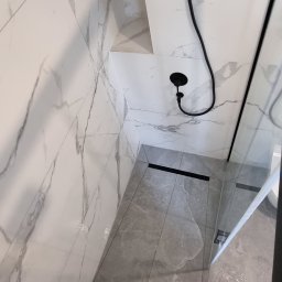 MEL- FI Remonty - Nowoczesna kabina prysznicowa z czarną armaturą, imitacją marmuru na ścianach i szarymi płytkami podłogowymi, widok z góry.