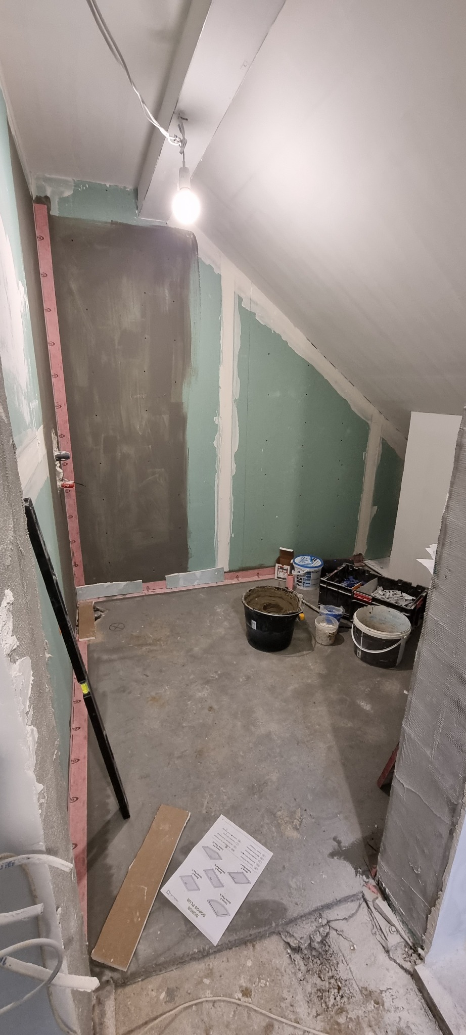 Poddasze w trakcie prac wykończeniowych: ściany z płyt gipsowo-kartonowych częściowo zagruntowane, widoczne wiadra z zaprawą, poziomica i instrukcja montażu.