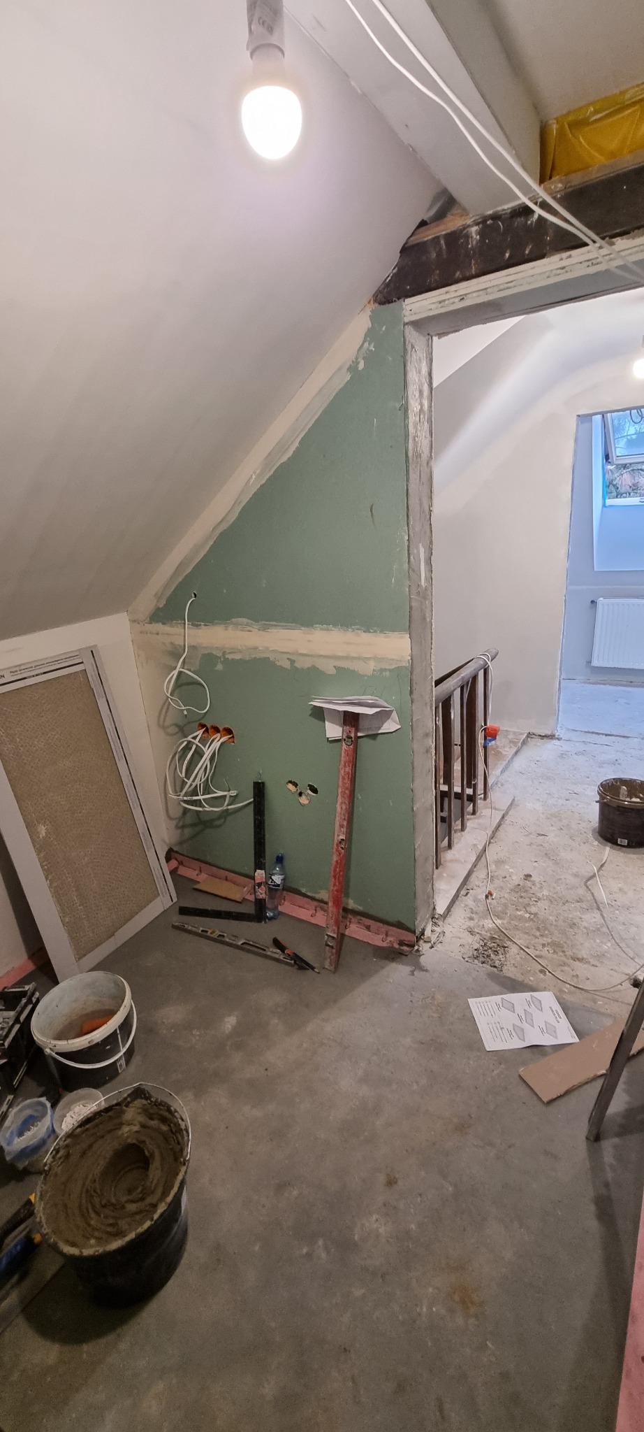 Poddasze w trakcie prac wykończeniowych: ściana z płyt gipsowo-kartonowych z widocznymi przewodami elektrycznymi, narzędzia, poziomica oparta o ścianę, wiadro z zaprawą i dokumentacja techniczna...