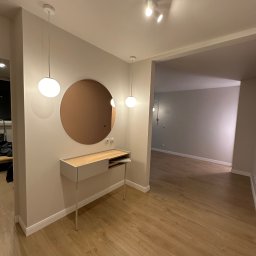 CORE PARTNER Bartłomiej Rejdych - Nowoczesny przedpokój z okrągłym lustrem w miedzianej ramie, minimalistyczną konsolą z jasnego drewna i białymi, kulistymi lampami wiszącymi, oświetlony reflektorami na szynie, z podłogą wyłożoną...