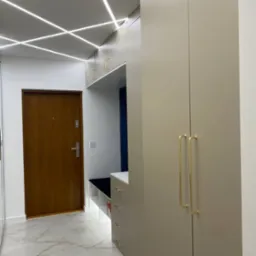 Nowoczesny przedpokój z szafą w zabudowie, siedziskiem i oświetleniem LED na suficie, marmurowa podłoga.