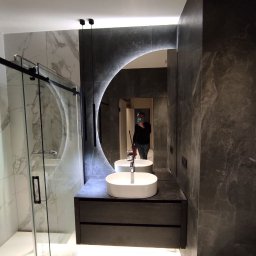 CORE PARTNER Bartłomiej Rejdych - Nowoczesna łazienka z marmurowymi płytkami, owalną umywalką nablatową i podświetlanym lustrem w kształcie półksiężyca, widoczna kabina prysznicowa ze szklanymi drzwiami.