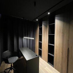 CORE PARTNER Bartłomiej Rejdych - Nowoczesne biuro z drewnianą podłogą, biurkiem w kolorze antracytowym z otworem na kable, krzesłem biurowym na kółkach i zabudową meblową z drewnopodobnymi frontami oraz czarnymi wnękami...