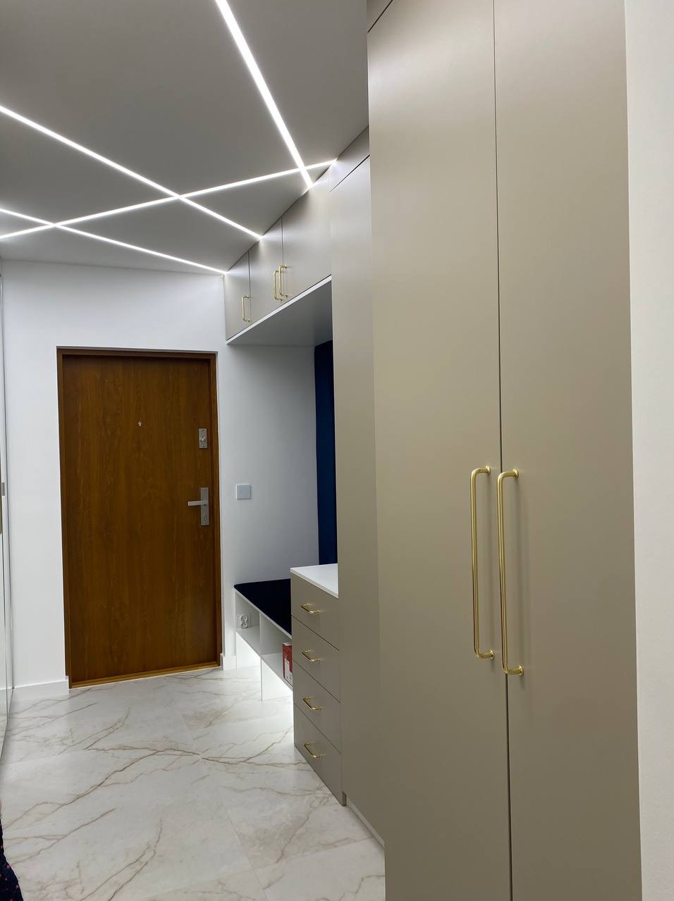 Nowoczesny przedpokój z szafą w zabudowie, siedziskiem i oświetleniem LED na suficie, marmurowa podłoga.