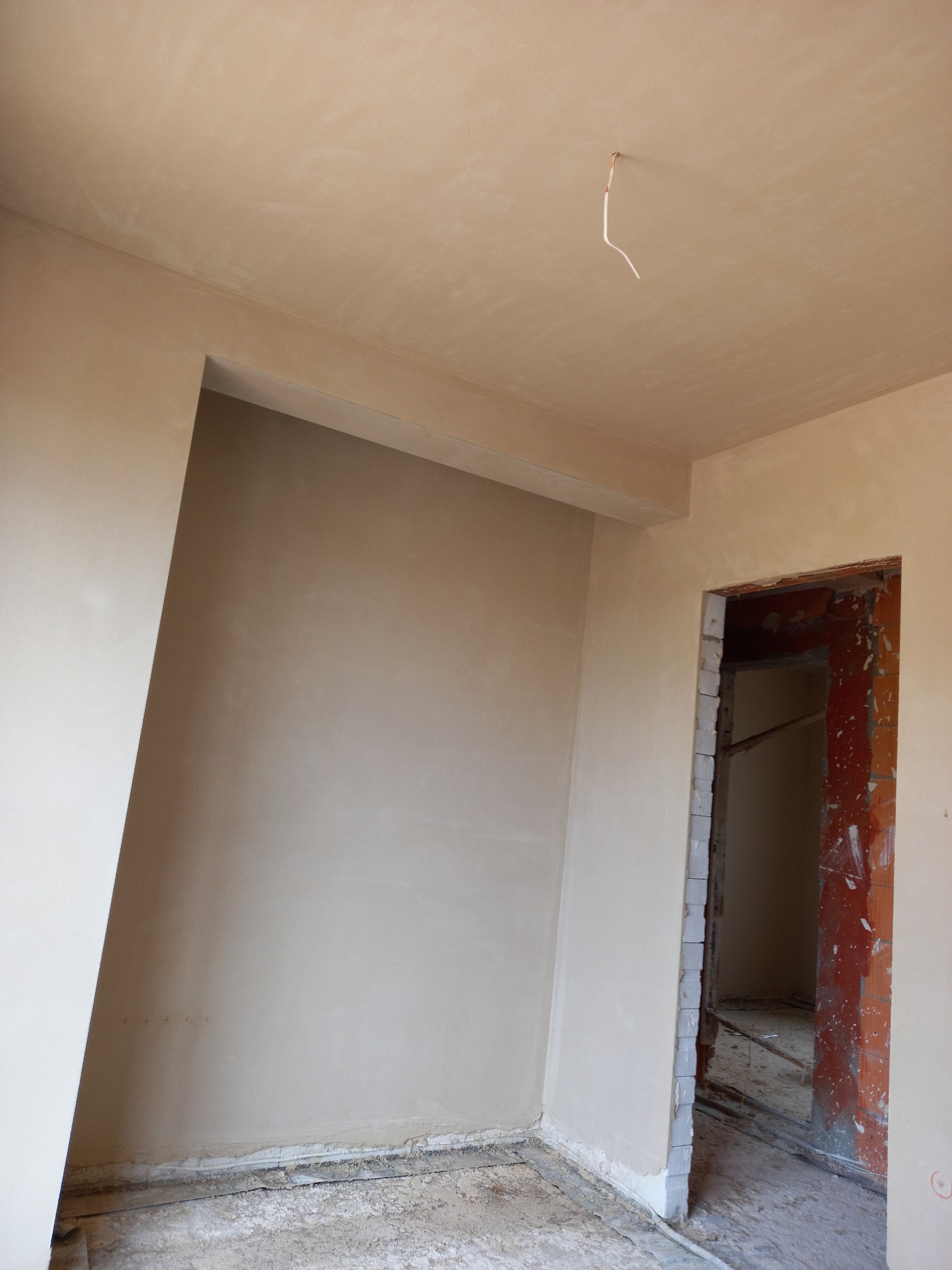 Wnętrze pomieszczenia po nałożeniu gładzi gipsowej, widoczne ślady po tynkowaniu przy podłodze i surowa ościeżnica drzwiowa.