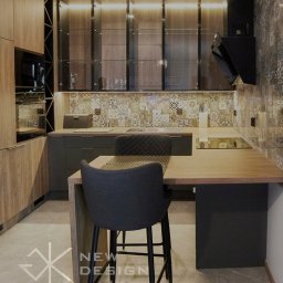 Meble New Design - Nowoczesna kuchnia z drewnianymi frontami szafek, czarnymi elementami i mozaiką nad blatem, oświetleniem LED podszafkowym i wysokim stołkiem barowym.