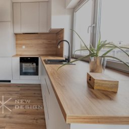 Meble New Design - Jasna kuchnia z drewnianym blatem, czarną armaturą i rośliną w srebrnej doniczce przy oknie, widok na zewnątrz.