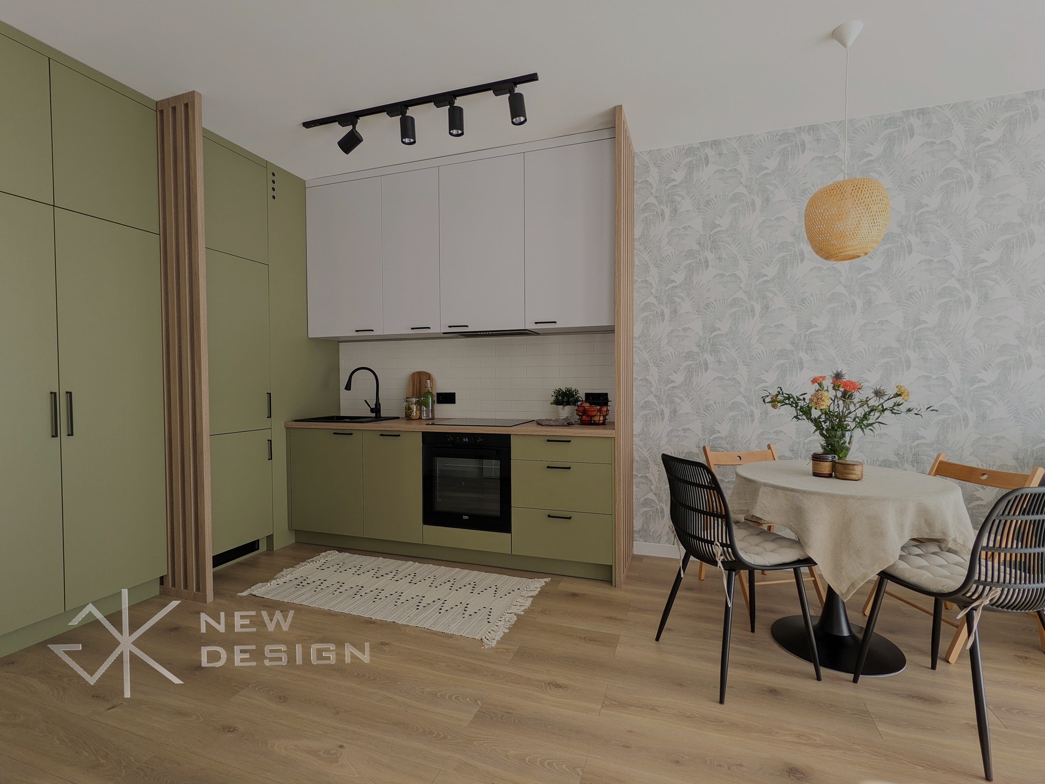Nowoczesna kuchnia z oliwkowymi szafkami, białymi górnymi szafkami i drewnianym panelem działowym, uzupełniona okrągłym stołem z kwiatami i rattanową lampą wiszącą.
