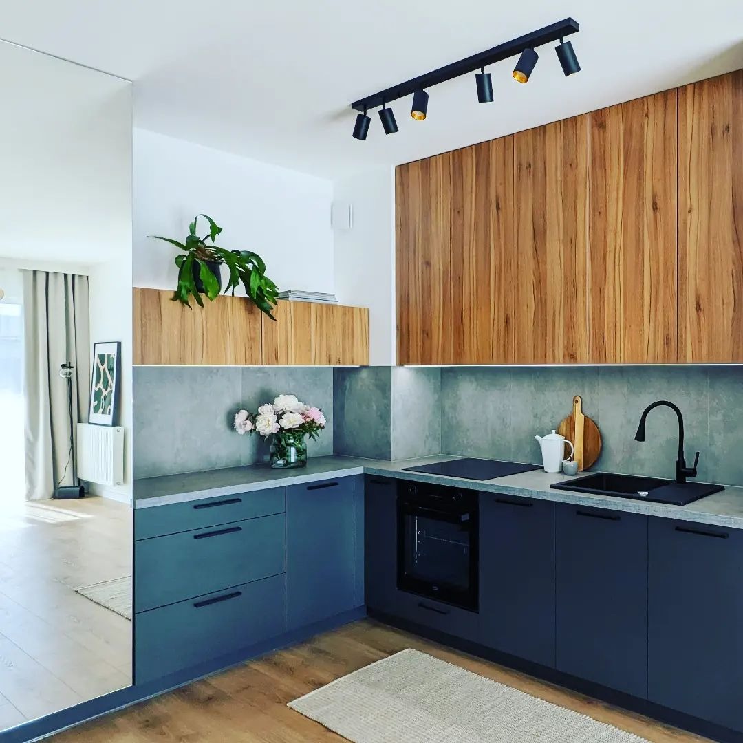 Nowoczesna kuchnia we Wrocławiu z szarymi frontami szafek, drewnianym blatem, czarną armaturą i oświetleniem punktowym, odbita w lustrzanej ścianie.