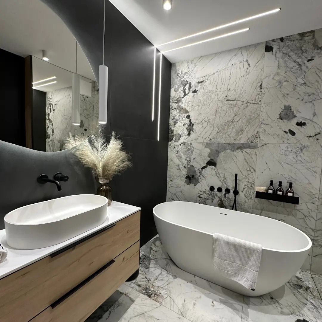 Nowoczesna łazienka z marmurowymi płytkami, wolnostojącą wanną, umywalką nablatową na drewnianej szafce, czarną armaturą i oświetleniem LED.