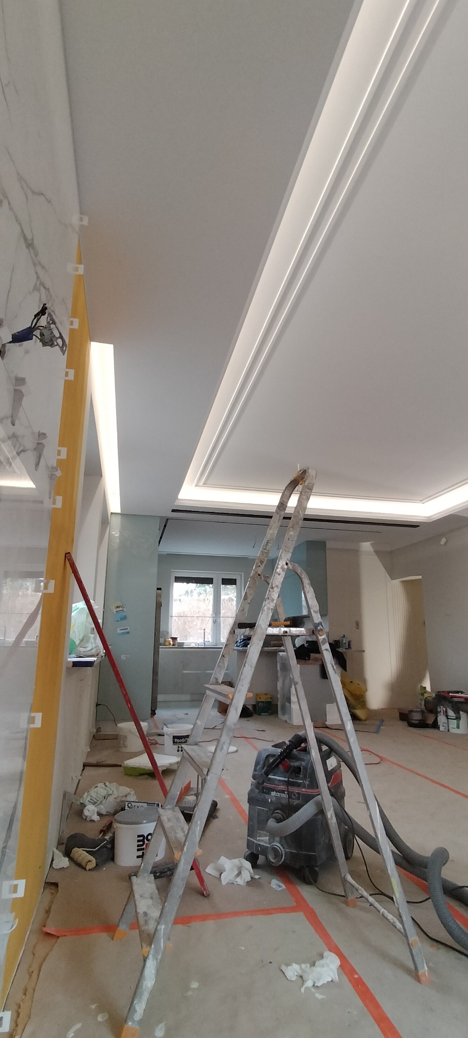 Wnętrze w trakcie prac wykończeniowych: położone płytki imitujące marmur na ścianie, sufit podwieszany z oświetleniem LED, drabina aluminiowa i odkurzacz przemysłowy.