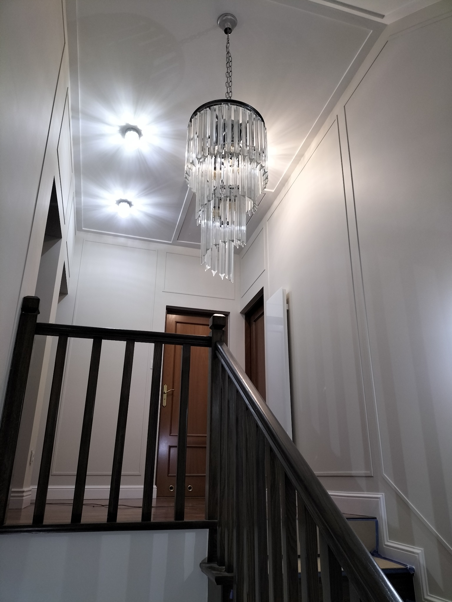 Klatka schodowa z drewnianą balustradą i kryształowym żyrandolem, ściany wykończone w białej sztukaterii.