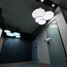 Nowoczesne oświetlenie sufitowe w kształcie chmury z okrągłych paneli LED, w minimalistycznym wnętrzu z szarą podłogą i ciemnymi drzwiami.