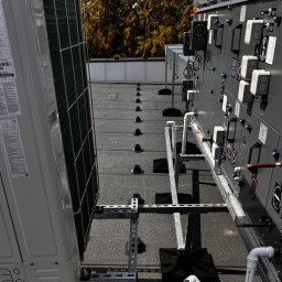 Kosztorysy i wykonawstwo Marcin Wróblewski - Sprzęt elektryczny na dachu budynku, w tym klimatyzator i panel sterowania z symbolami elektrycznymi i rurami, zamontowany na metalowej konstrukcji wsporczej.