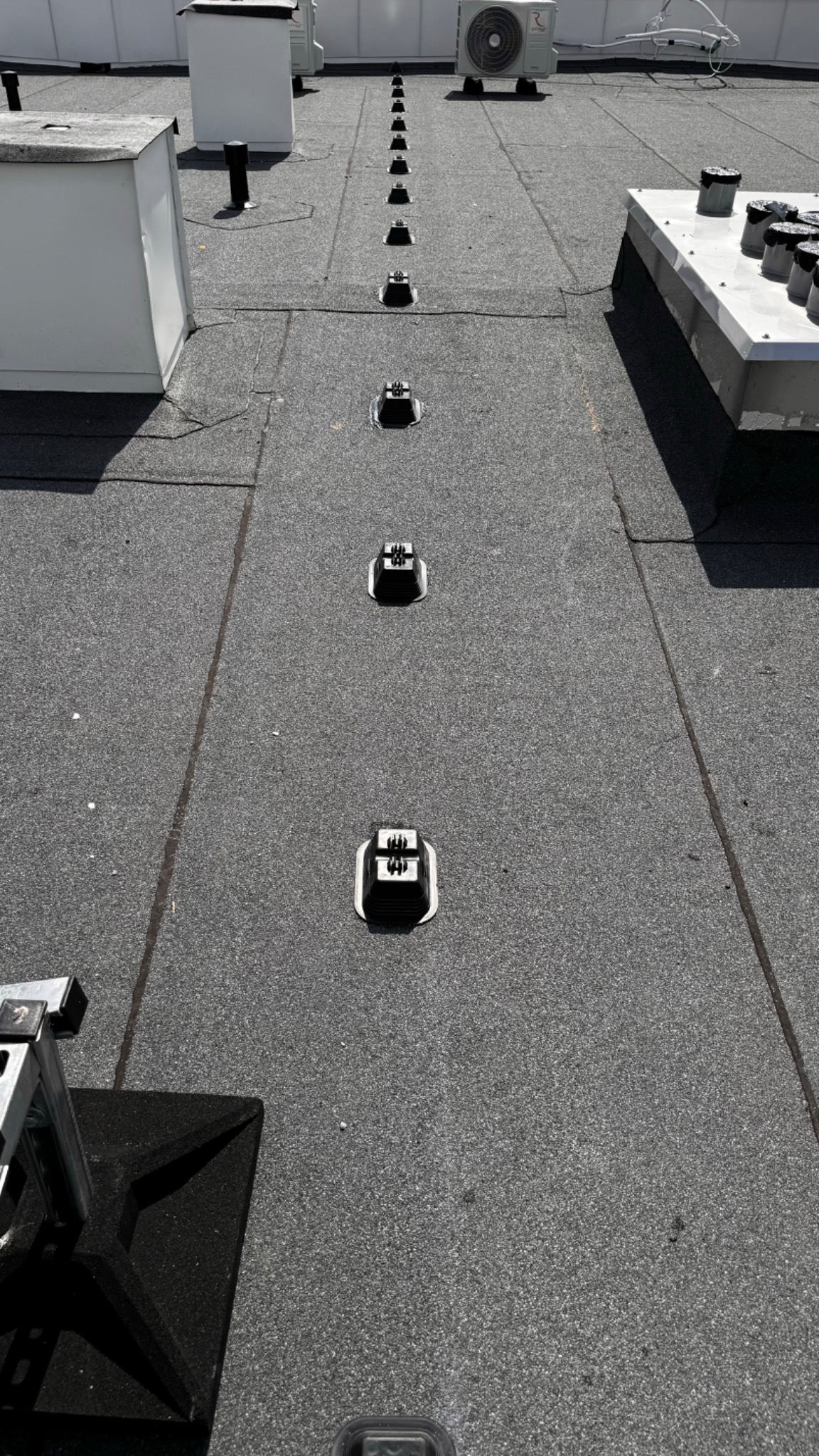 Szereg uchwytów odgromowych zamontowanych na płaskim dachu pokrytym papą, widoczne klimatyzatory w tle.