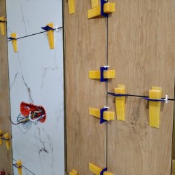 PCmedia24 Szczepan Jasiński - Układanie płytek imitujących drewno i marmur z użyciem systemu poziomowania. Widoczne kable w puszce elektrycznej. Detal z bliska, oświetlenie naturalne.