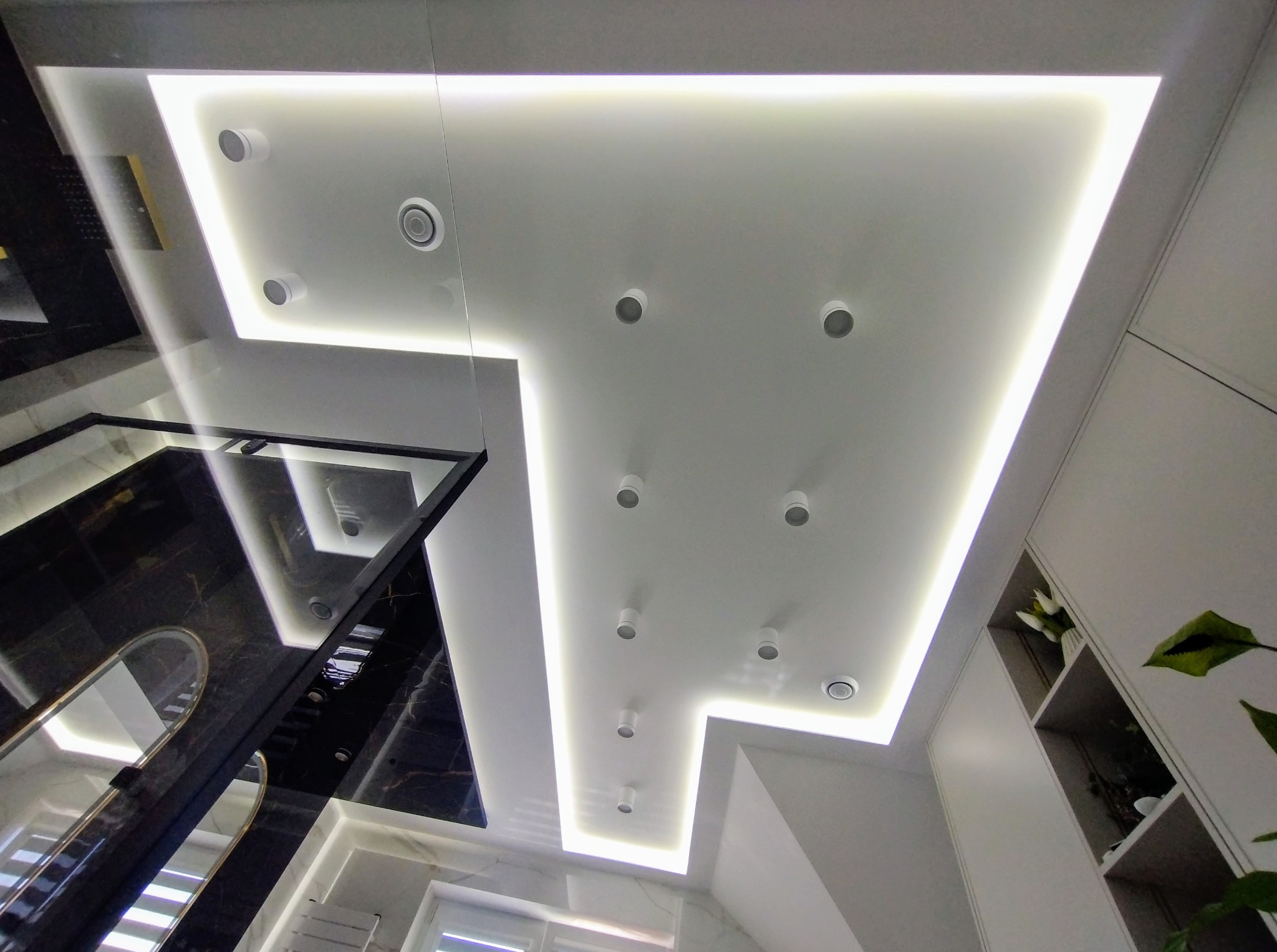 Nowoczesny sufit podwieszany z oświetleniem LED i punktowymi lampami w łazience. Geometryczny kształt, białe wykończenie, widok z dołu.