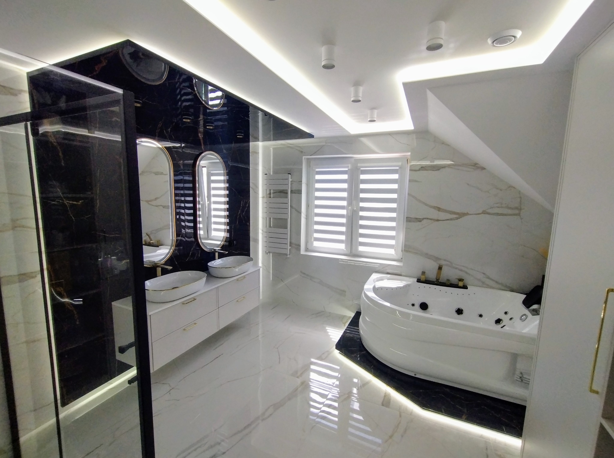 Nowoczesna łazienka na poddaszu z wanną z hydromasażem, umywalkami nablatowymi i kabiną prysznicową typu walk-in, wykończona marmurem i podświetleniem LED.