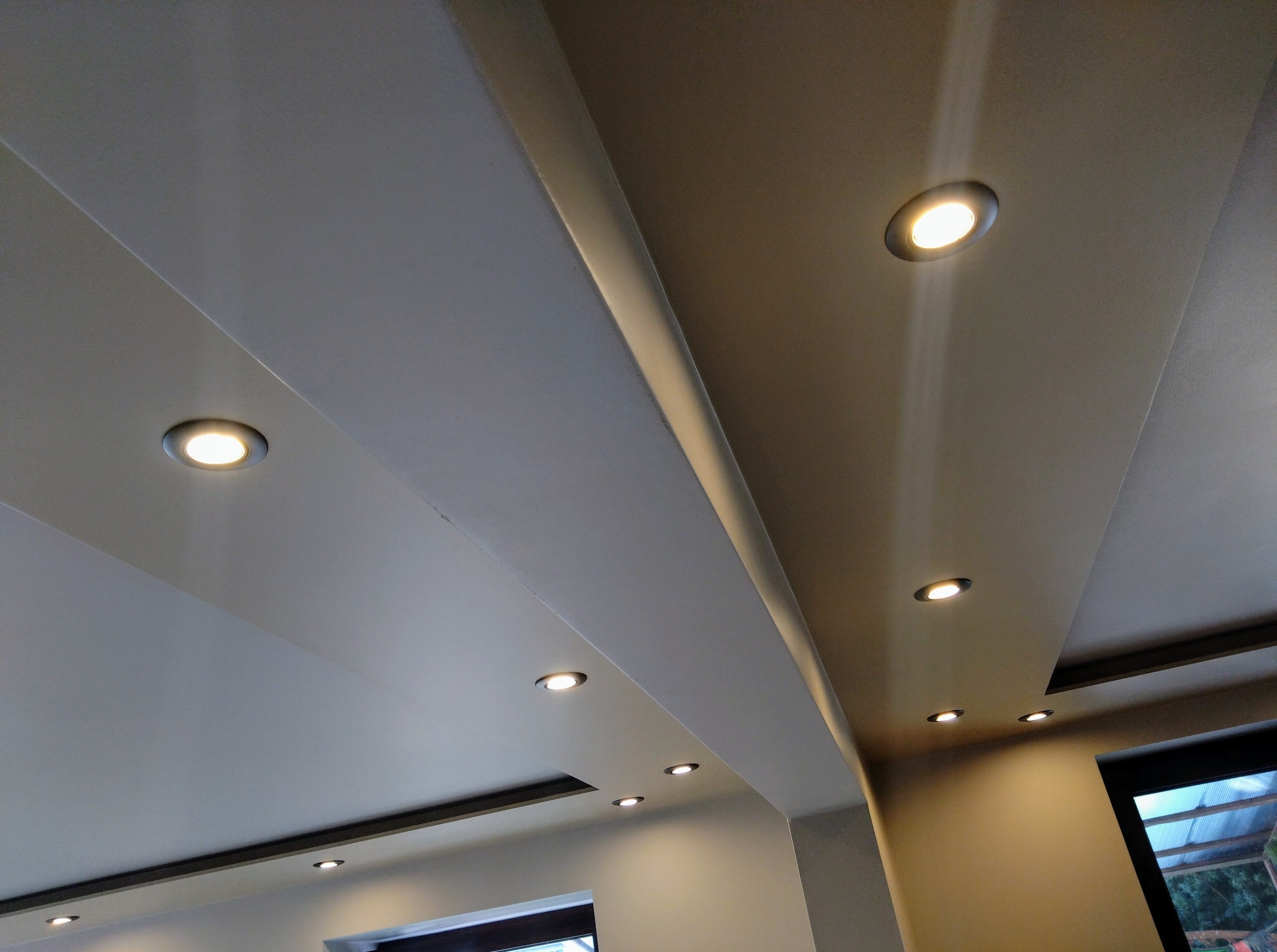 Nowoczesny sufit podwieszany z oświetleniem punktowym LED, widok z dołu, neutralna kolorystyka ścian i sufitu, minimalistyczny design.