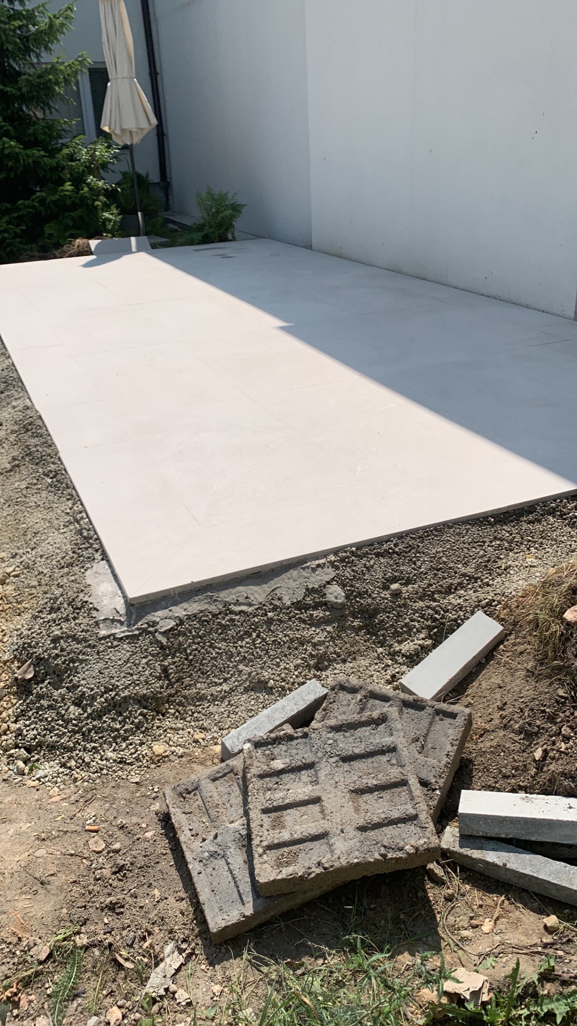 Ułożona jasna kostka brukowa na przygotowanym podłożu, widoczne stare, szare płyty chodnikowe i obrzeża. Prace brukarskie w toku, widok z góry.