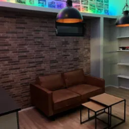 Salon z ceglaną ścianą, brązową sofą, drewnianymi stolikami i oświetleniem w stylu industrialnym, podświetlona p&oacute;łka z modelami samochod&oacute;w pod sufitem.